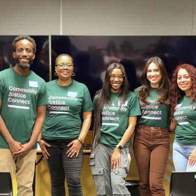 Seven people stand together in a row with green and pink Community Justice Connect shirts on