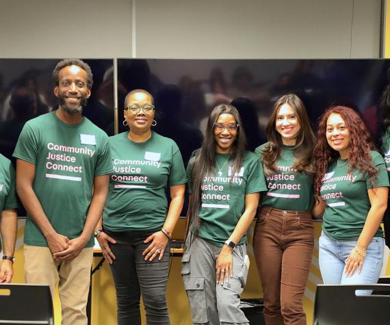 Seven people stand together in a row with green and pink Community Justice Connect shirts on