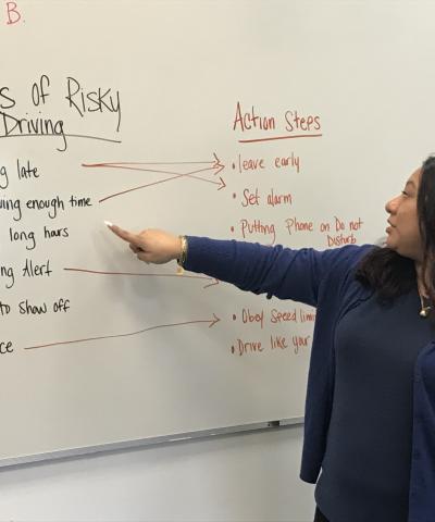 Facilitator at Driver Accountability Program stands before whiteboard displaying causes and solutions to risky driving.