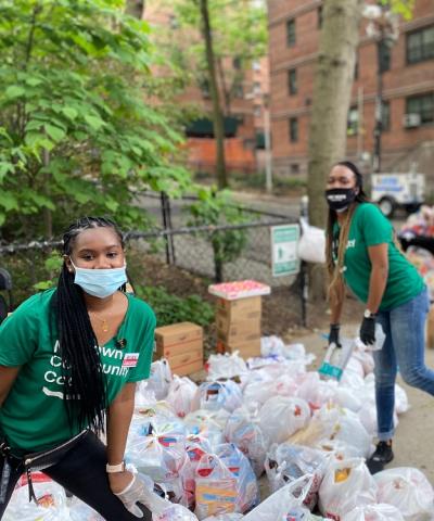 Three women in masks and green t-shirts that say Midtown Community Court distribute supplies to the community