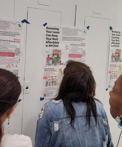 Three people reading NYCHA tenant guide posters on wall.