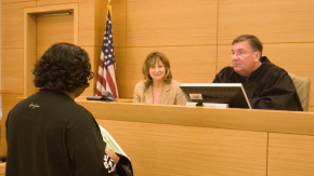 Judge D'emic and a colleague sit at the court bench speaking to a participant in black clothing