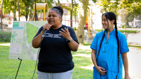 Two members of our Neighborhood Safety Initiatives team speak at the opening of the new dog park in the Castle Hill Houses in front of the blueprint for the new green space.