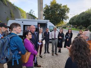 Group of harm reduction staff stand on side of street in front of a van, listening to a presentation