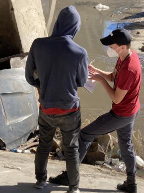 Two harm reduction staff stand outside in front of a stone wall, discussing plans