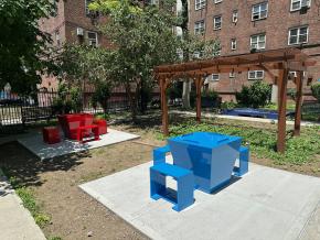 Patterson Houses community garden with "Serenity Tables," one bright red and one bright blue geometric table with rectangular benches.