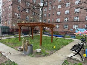 Patterson Houses community garden before addition of Serenity Tables, featuring a square grass area with a wooden arbor.