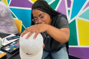 Team member from our Staten Island Justice Center at a face-painting station with a young child at our Family Enrichment Center.