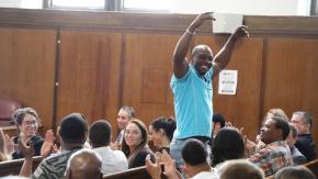 Man celebrating with arms up and crown applauding at a ceremony