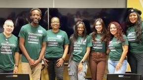 Seven people stand together in a row with green and pink Community Justice Connect shirts on