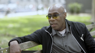 Middle-aged man with yellow sunglasses and a button-down shirt on a park bench during the day.