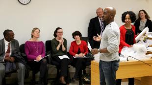 A man in sweater and jeans speaks in front of a group of people smiling